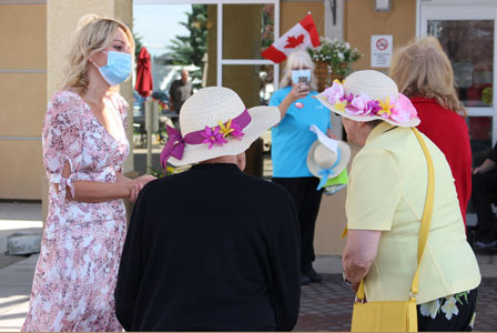 Mayor wearing a mask while talking with a group of senior ladies all wearing hats